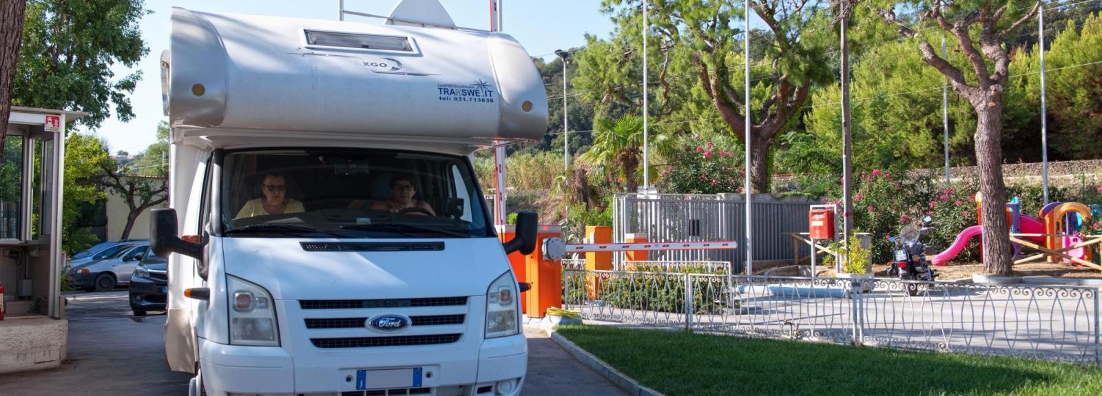 Camper bianco in uscita da un campeggio con parco giochi.
