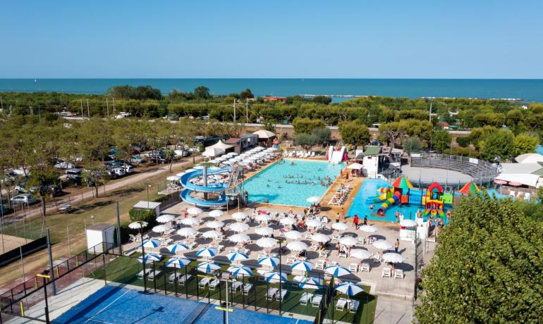 Piscina con scivoli e vista mare, ombrelloni e campo sportivo.