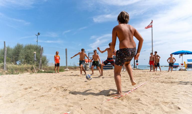 Ragazzi giocano a calcio sulla spiaggia con il sole estivo.