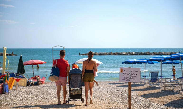 Famille sur une plage libre à Fermo, parasols et mer.