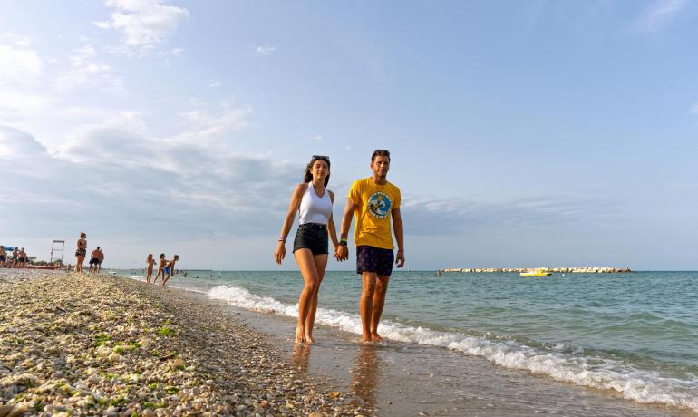 Couple heureux marche sur la plage, vagues douces, ciel dégagé.
