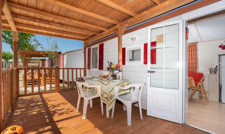Veranda in legno con tavolo e sedie, accanto a una casa mobile.