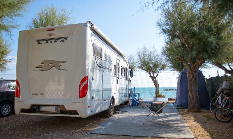 Camping-car garé près de la mer, entouré d'arbres et de vélos.