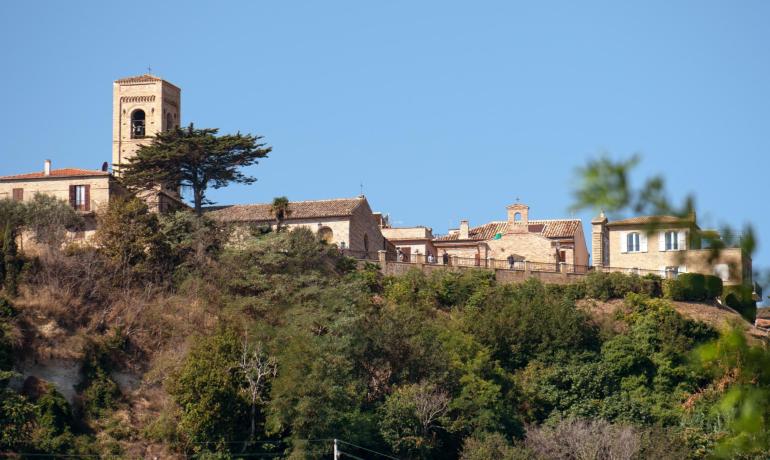 Paesaggio collinare con chiesa e case storiche.