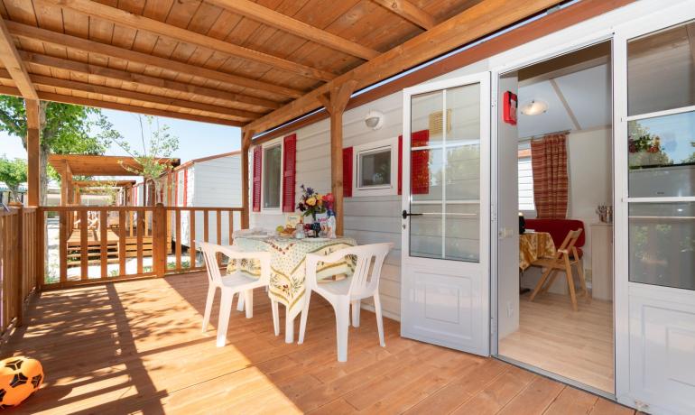 Terrazza in legno con tavolo apparecchiato e sedie bianche.
