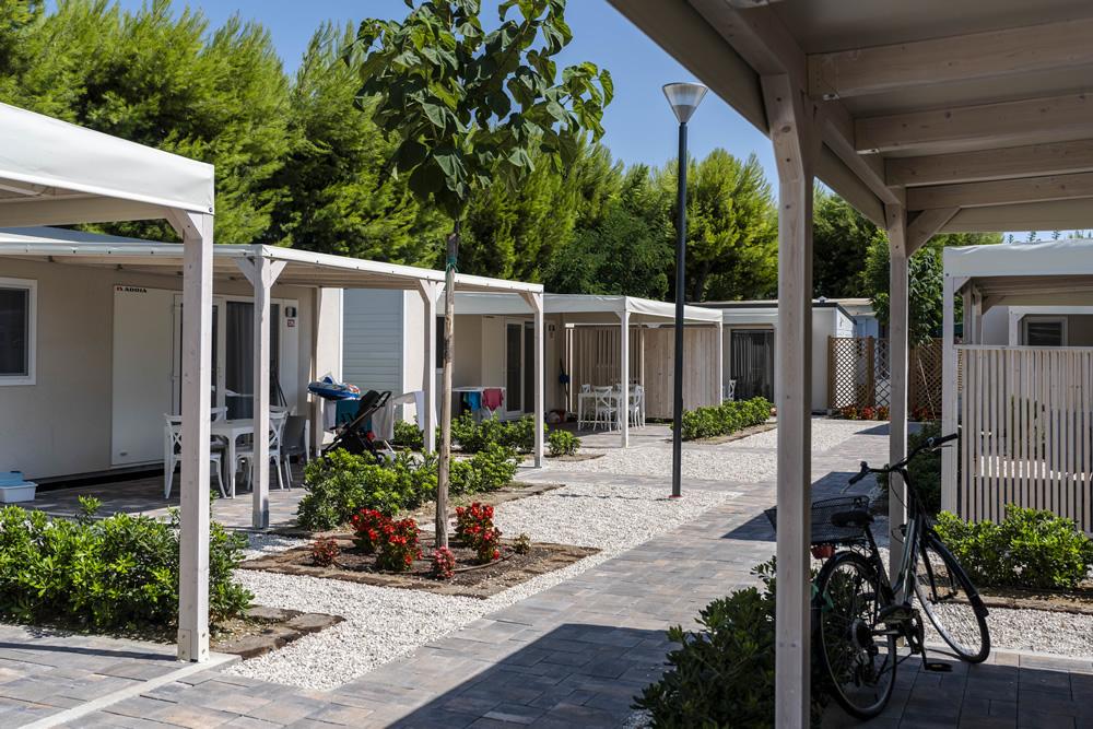 Villaggio turistico con bungalow, giardini curati e biciclette parcheggiate.