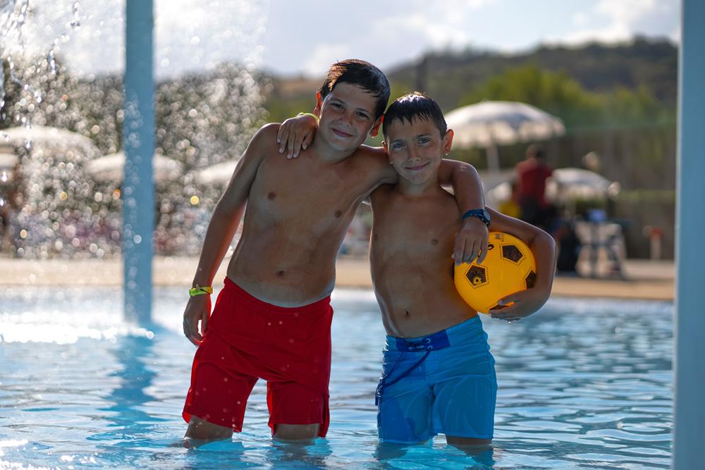 Due ragazzi in piscina con un pallone giallo.