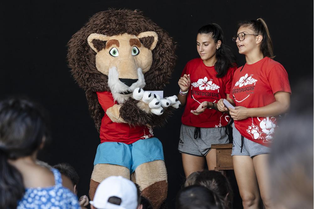 Mascotte leone e due animatrici interagiscono con bambini.