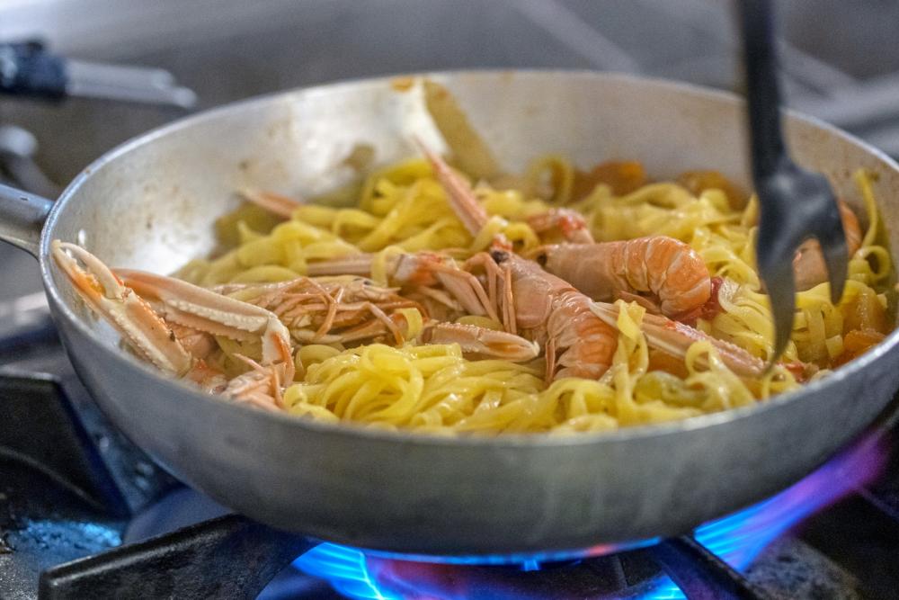 Tagliatelle ai gamberi in padella su fornello acceso.