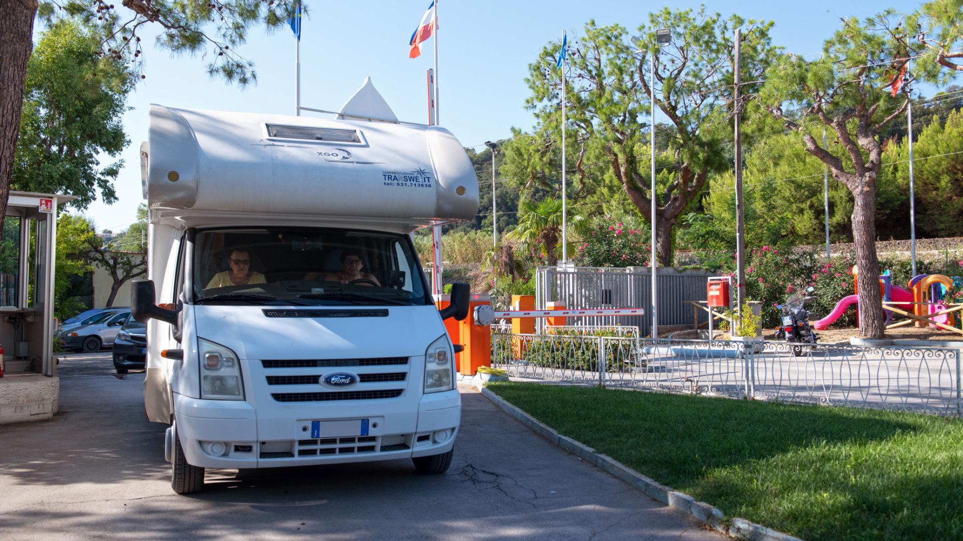 Camper bianco esce da un campeggio con parco giochi.