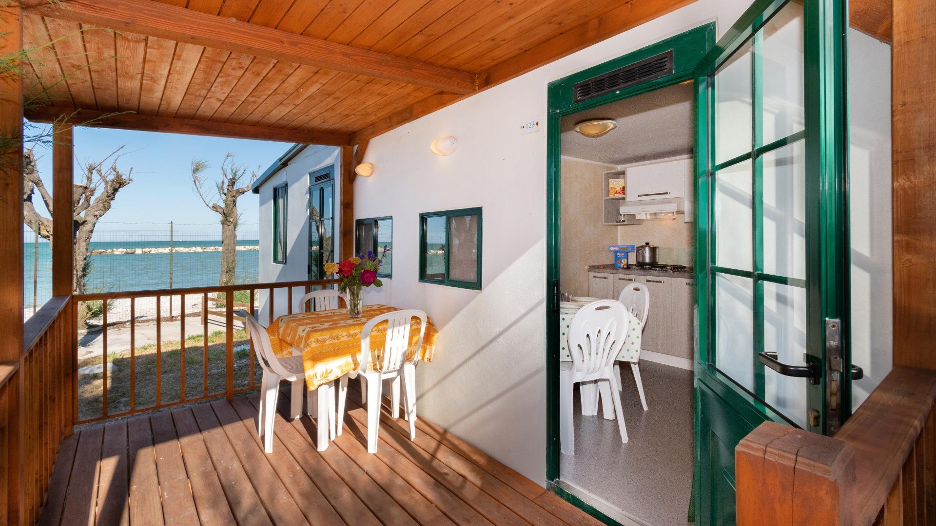 Terrasse en bord de mer avec table à manger et cuisine intérieure.