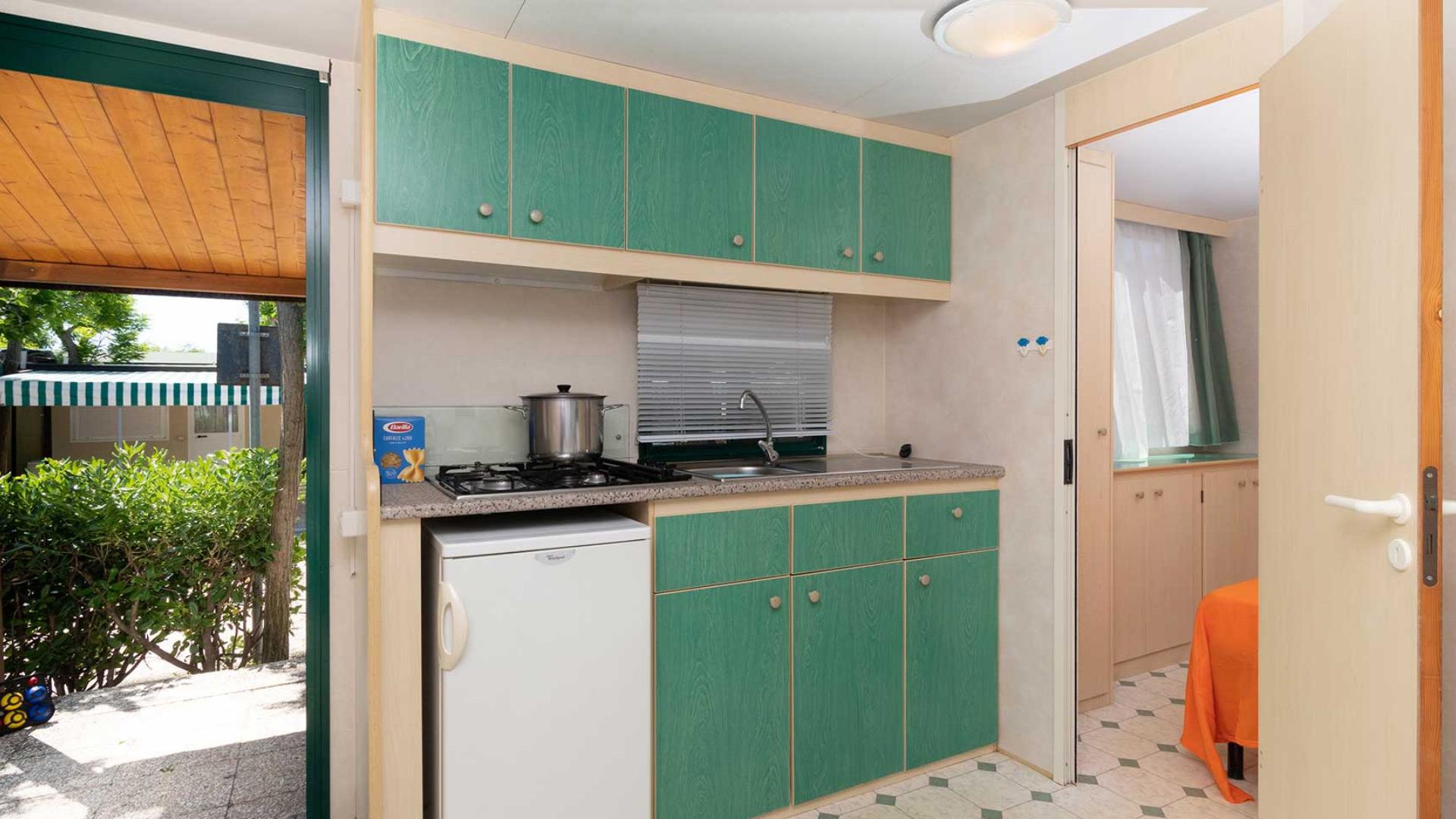 Cucina compatta con mobili verdi e vista giardino.