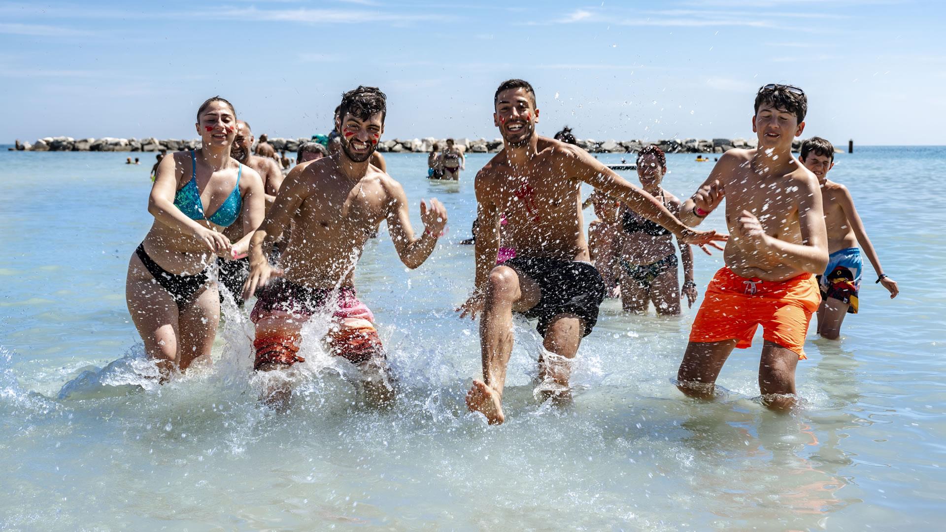 Gruppo di amici felici che corrono in acqua al mare.