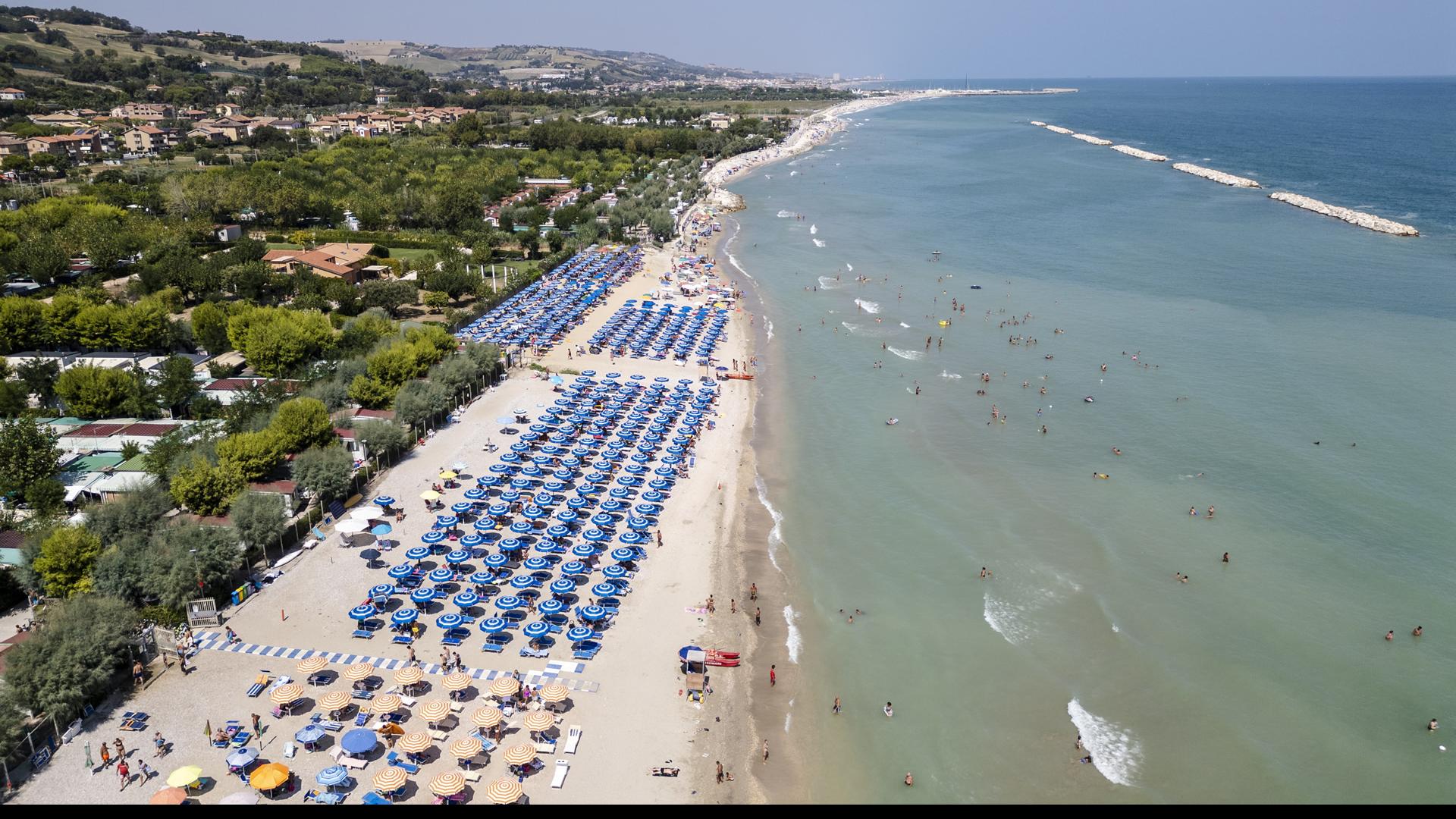 Spiaggia affollata con ombrelloni blu e mare calmo.