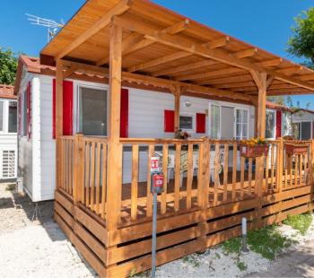 Casa mobile con veranda in legno, circondata da alberi.