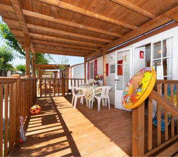 Veranda in legno con tavolo, sedie e giochi per bambini.