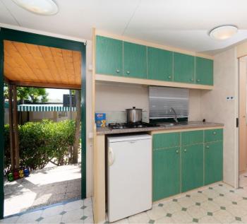 Piccola cucina con mobili verdi, frigorifero e piano cottura.