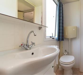 Bagno compatto con lavabo e wc, finestra e tenda blu.