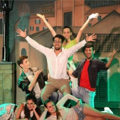 Gruppo di persone in posa teatrale su sfondo scenografico.
