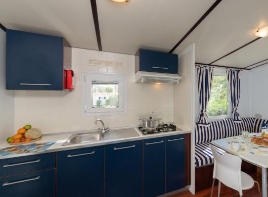 Cucina compatta con tavolo, sedie e tende a righe blu.