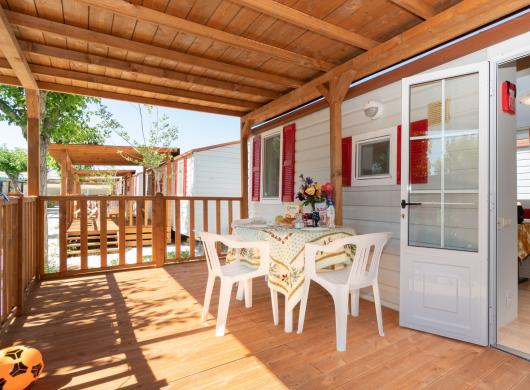 Veranda in legno con tavolo apparecchiato e sedie bianche.