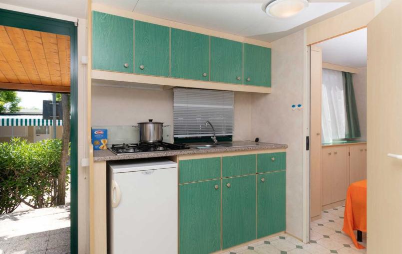 Cucina compatta con mobili verdi e vista giardino.