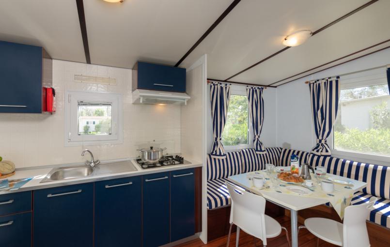 Cucina compatta con tavolo, sedie e tende a righe blu.