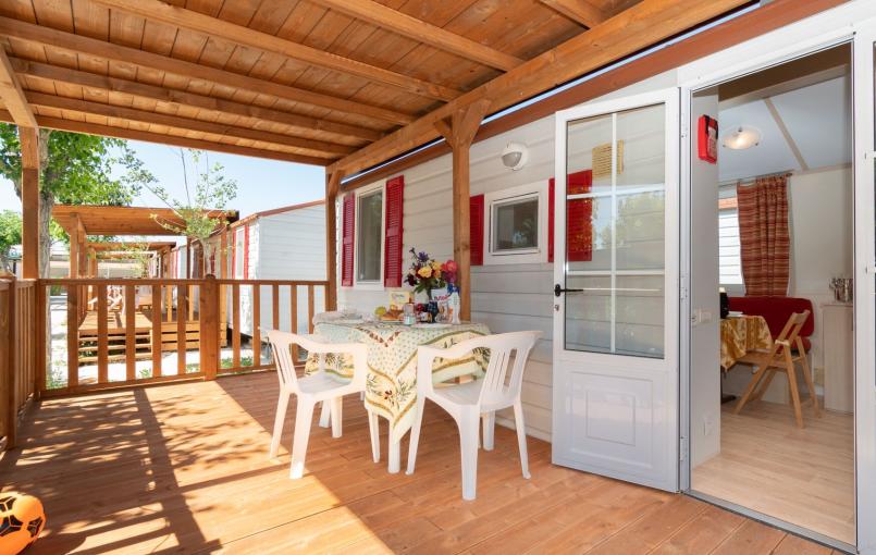 Veranda in legno con tavolo apparecchiato e sedie bianche.